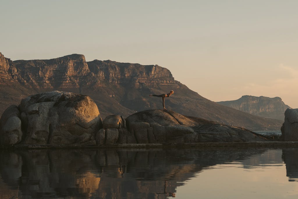 Woman practicing yoga on boulders during sunset in Cape Town, reflecting a serene wellness moment.